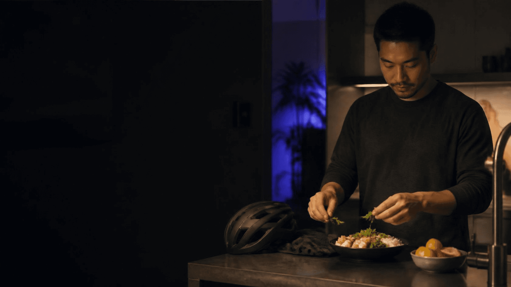 Un homme rentré à vélo, casque posé sur le plan de travail, garnit une assiette simple dans sa cuisine.