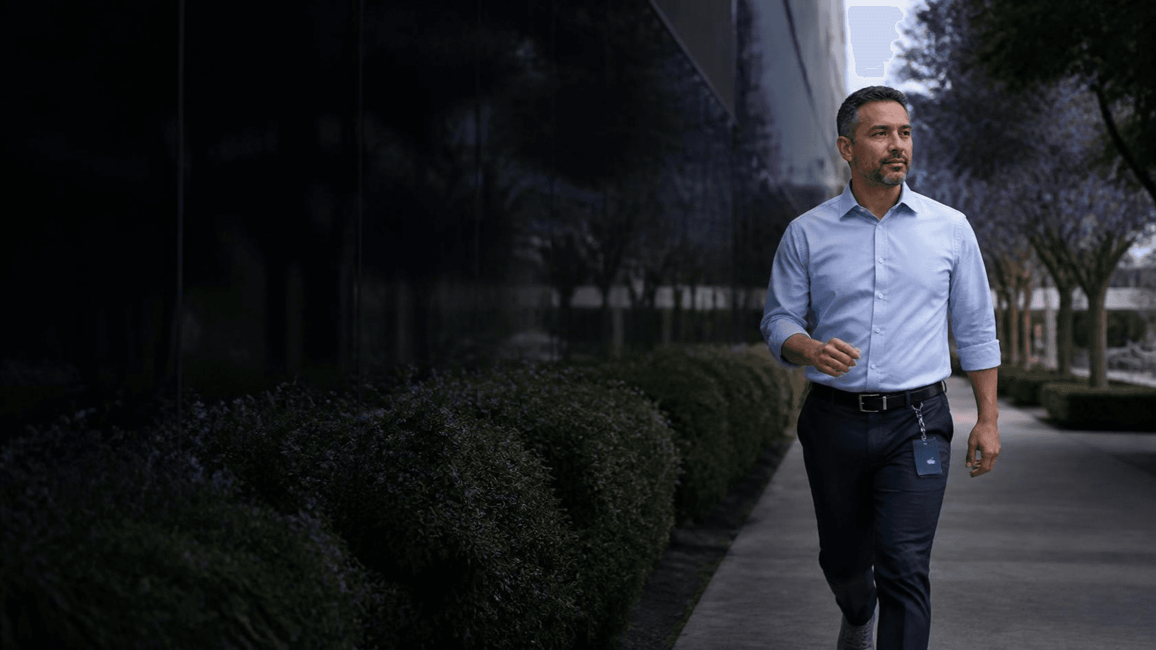 Un homme en chemise marche d'un pas soutenu le long d'un immeuble de bureaux pendant sa pause.